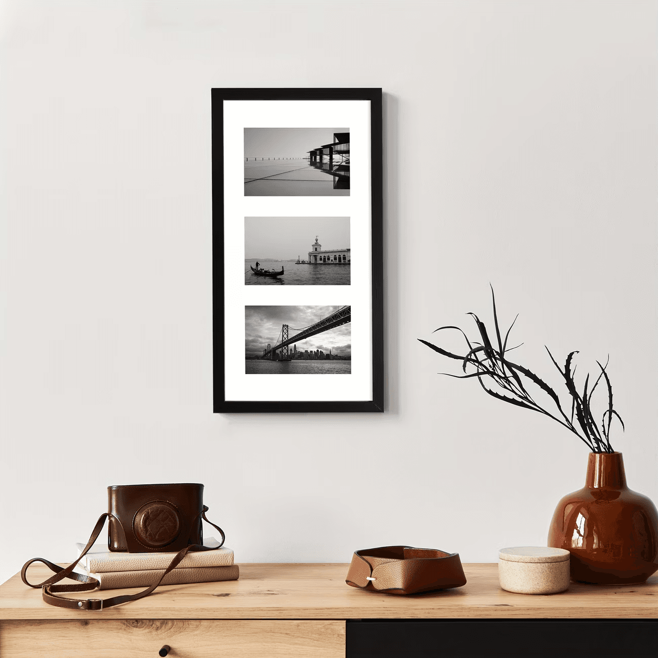 A black triple frame of black and white travel photos above a desk